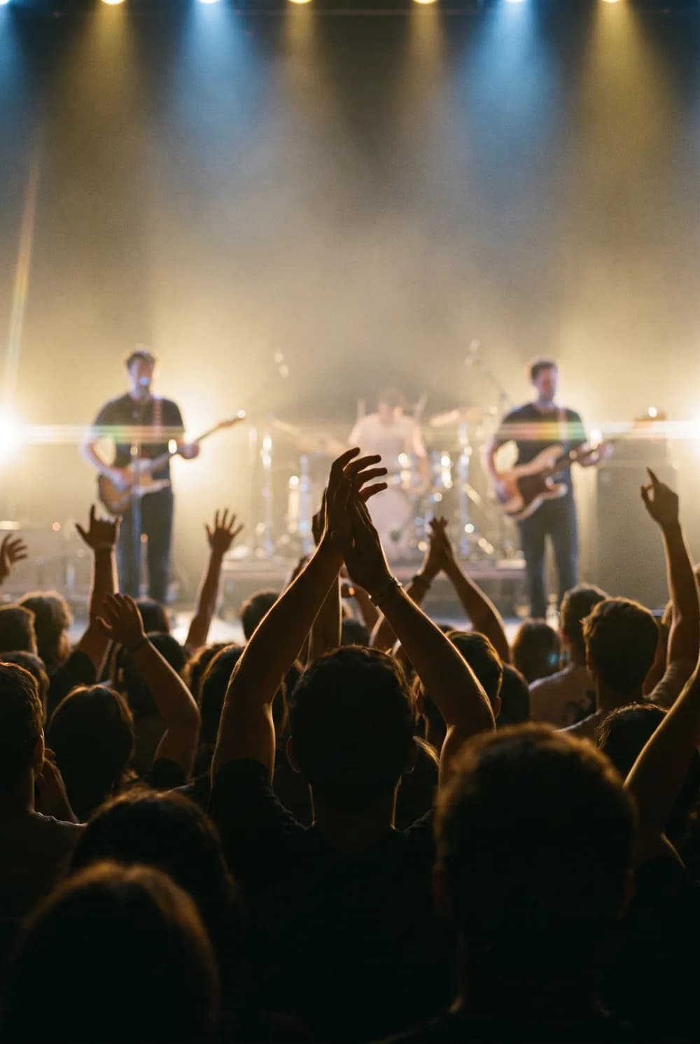 A packed crowd with hands raised, lit gold by the stage at a live show