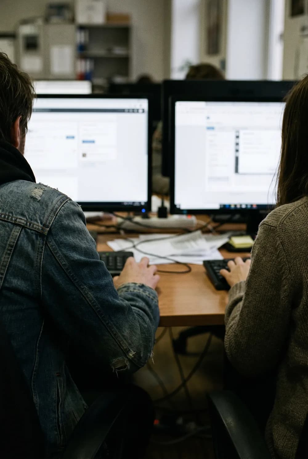 Two colleagues working side by side at a desk, seen from behind